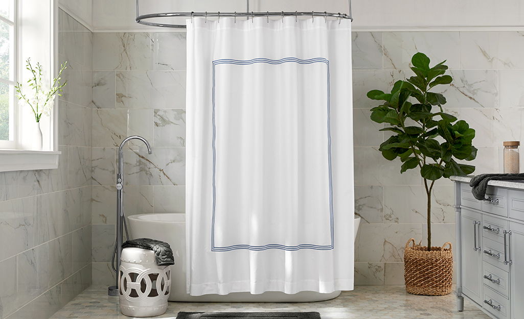 A white shower curtain hanging in a marble bath.