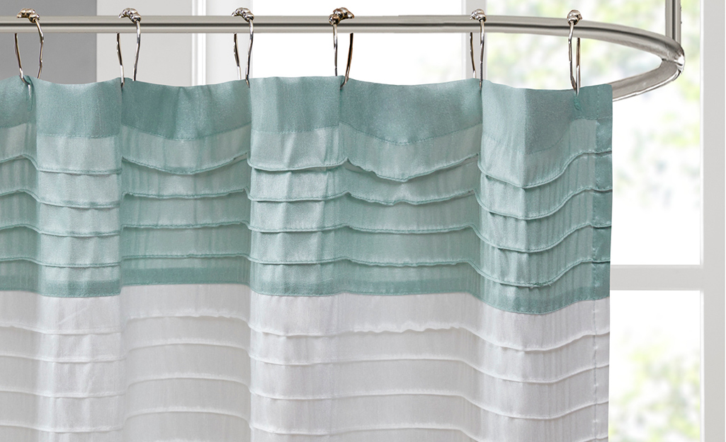A shower curtain with a teal stripe hanging on a circular shower rod.