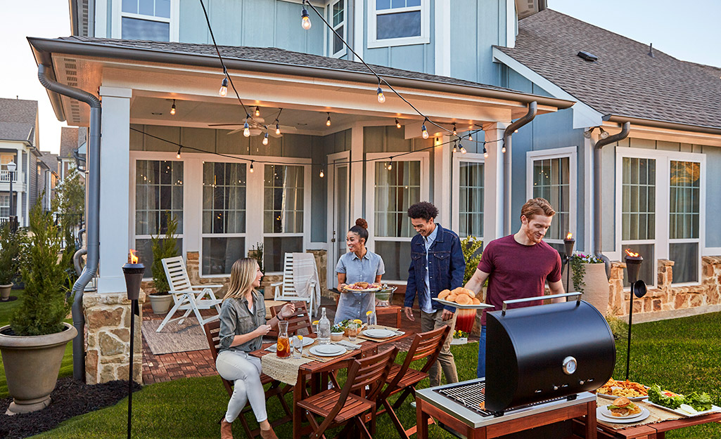 Four friends gather in a backyard around a grill and outdoor seating for a cookout.