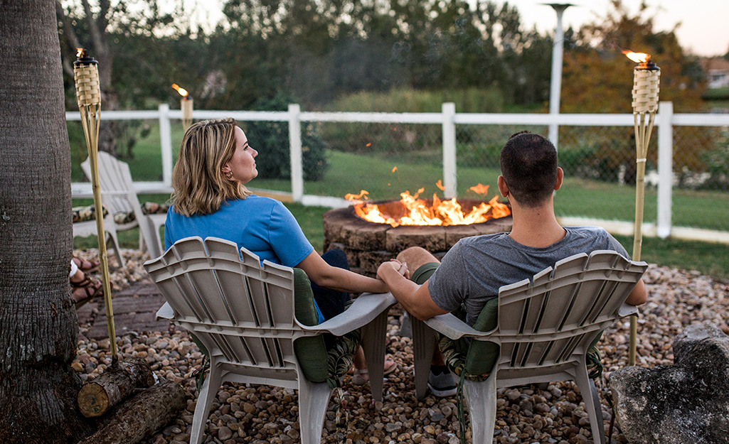 Two people sit by a fire pit in the evening.