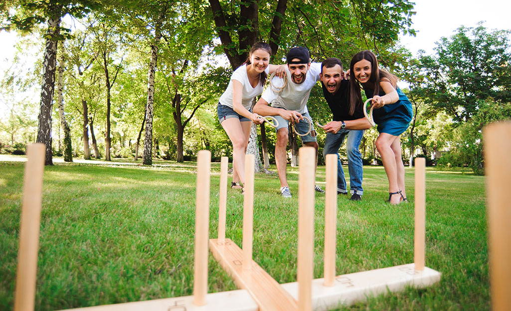 Four people play ring toss in a backyard.