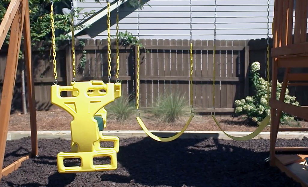 A wooden swing set with yellow swings and a seesaw swing.