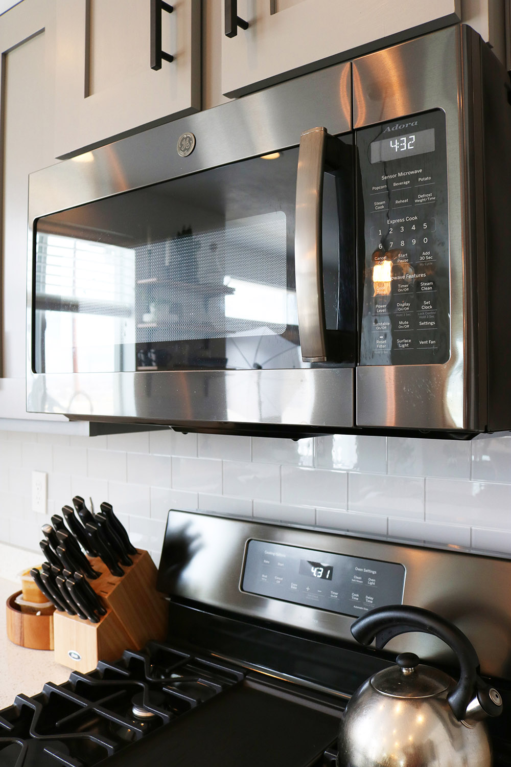 A GE black stainless steel microwave hangs over a gas range.