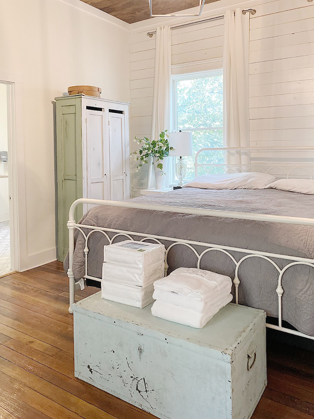 A bedroom with a white iron bed sitting in front of a shiplap accent wall.