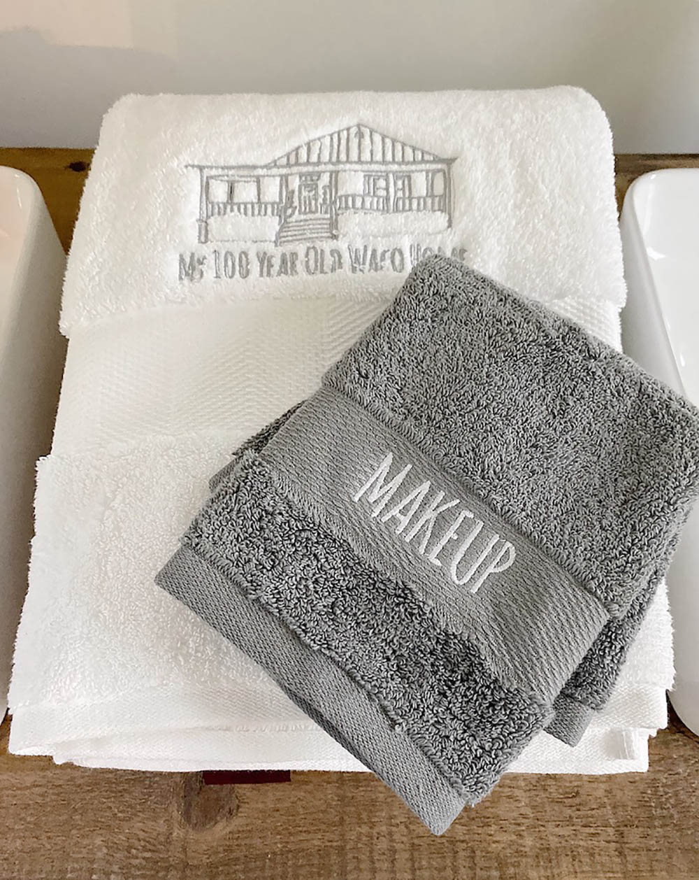 A gray washcloth with the word makeup embroidered on it sits on top of a white personalized hand towel.