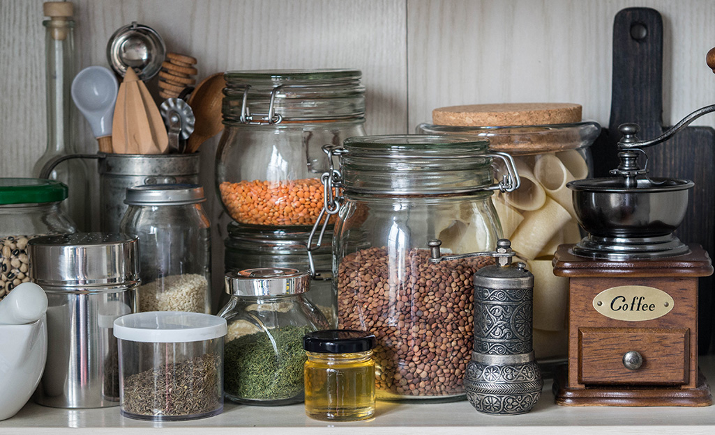 Spices in transparent containers stand alongside utensils and other items on a pantry shelf.