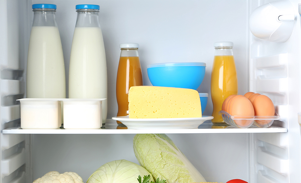 Milk, eggs, butter and other dairy products stand on a shelf in a refrigerator.