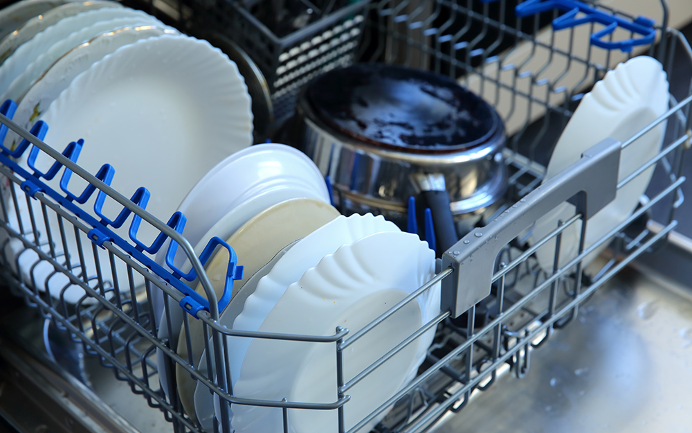 The bottom rack of a dishwasher full of plates and a pot.