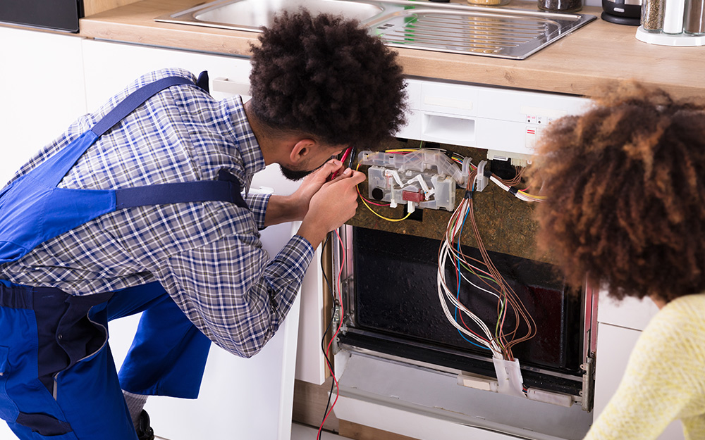 Two people look at the electrical components of a dishwasher.