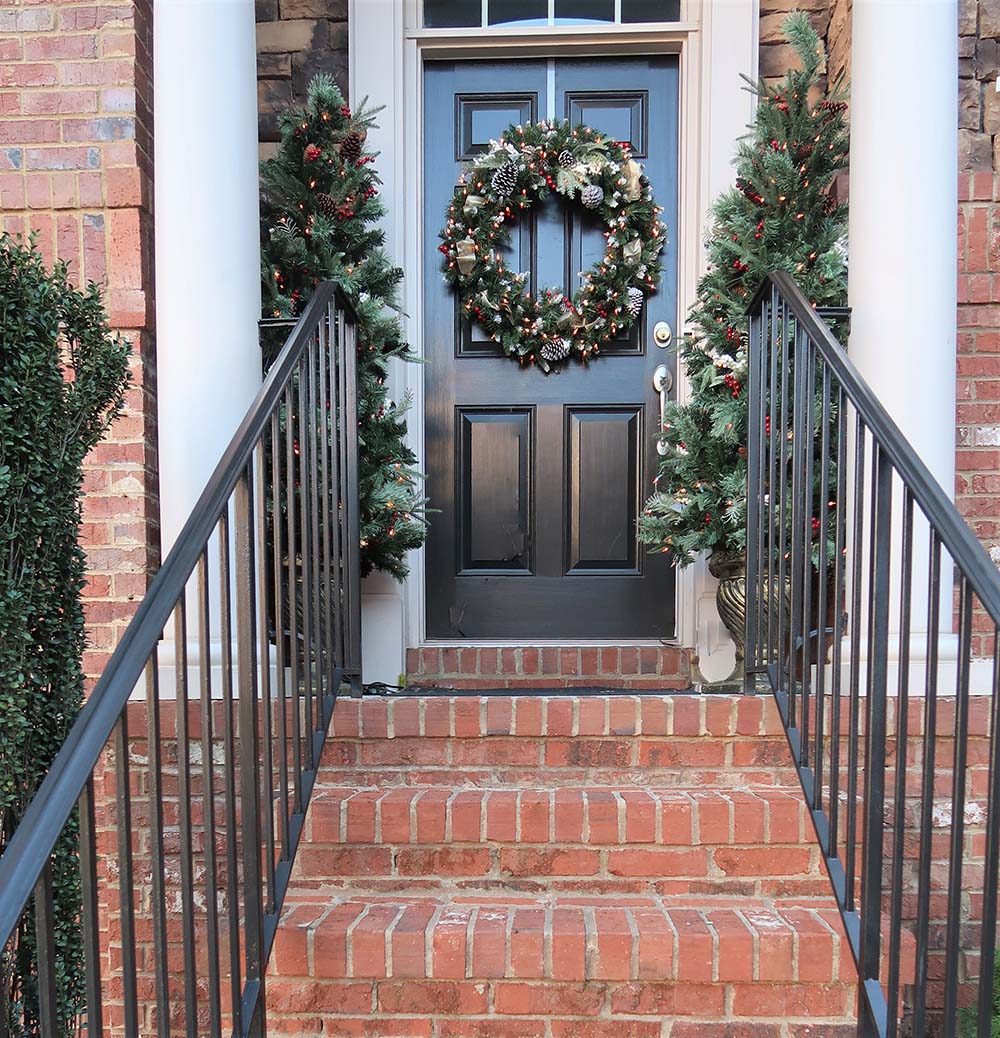 A brick stairway leads to a black front door decorated with a Christmas wreath.