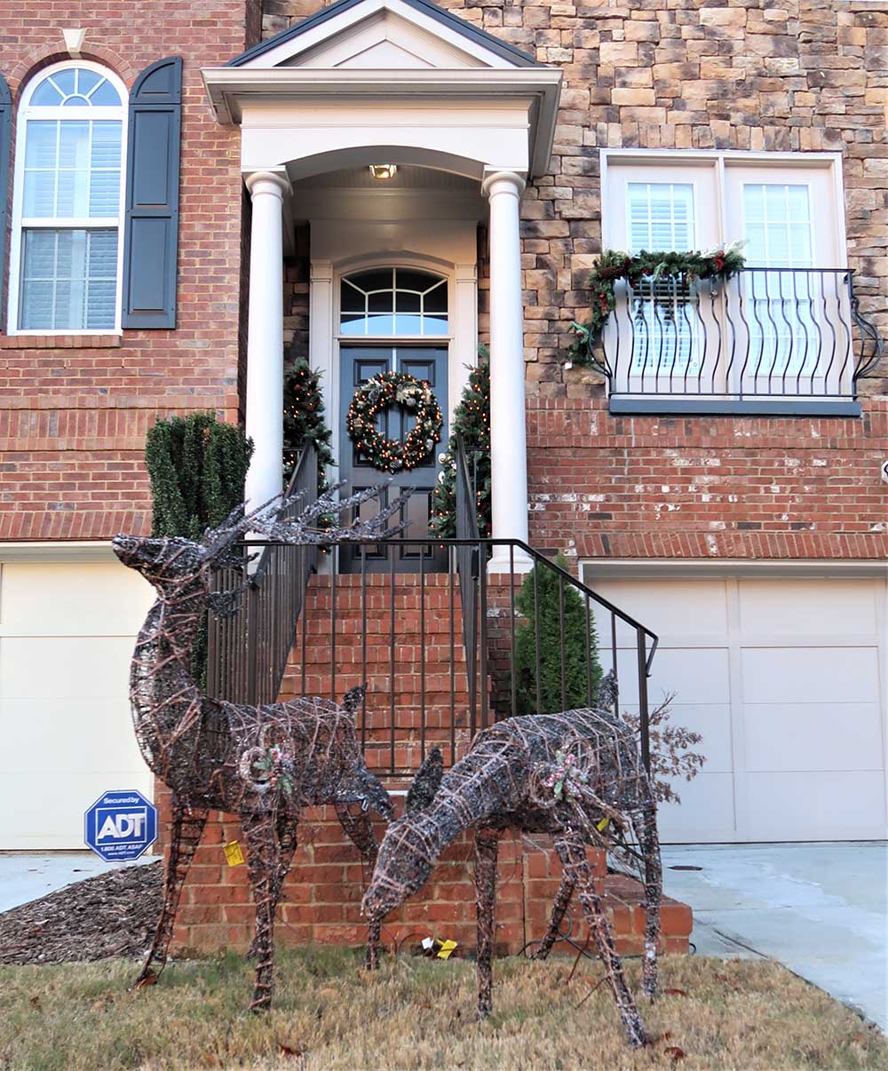 The exterior of a townhouse decorated for Christmas with wreaths, garland, and LED deer.