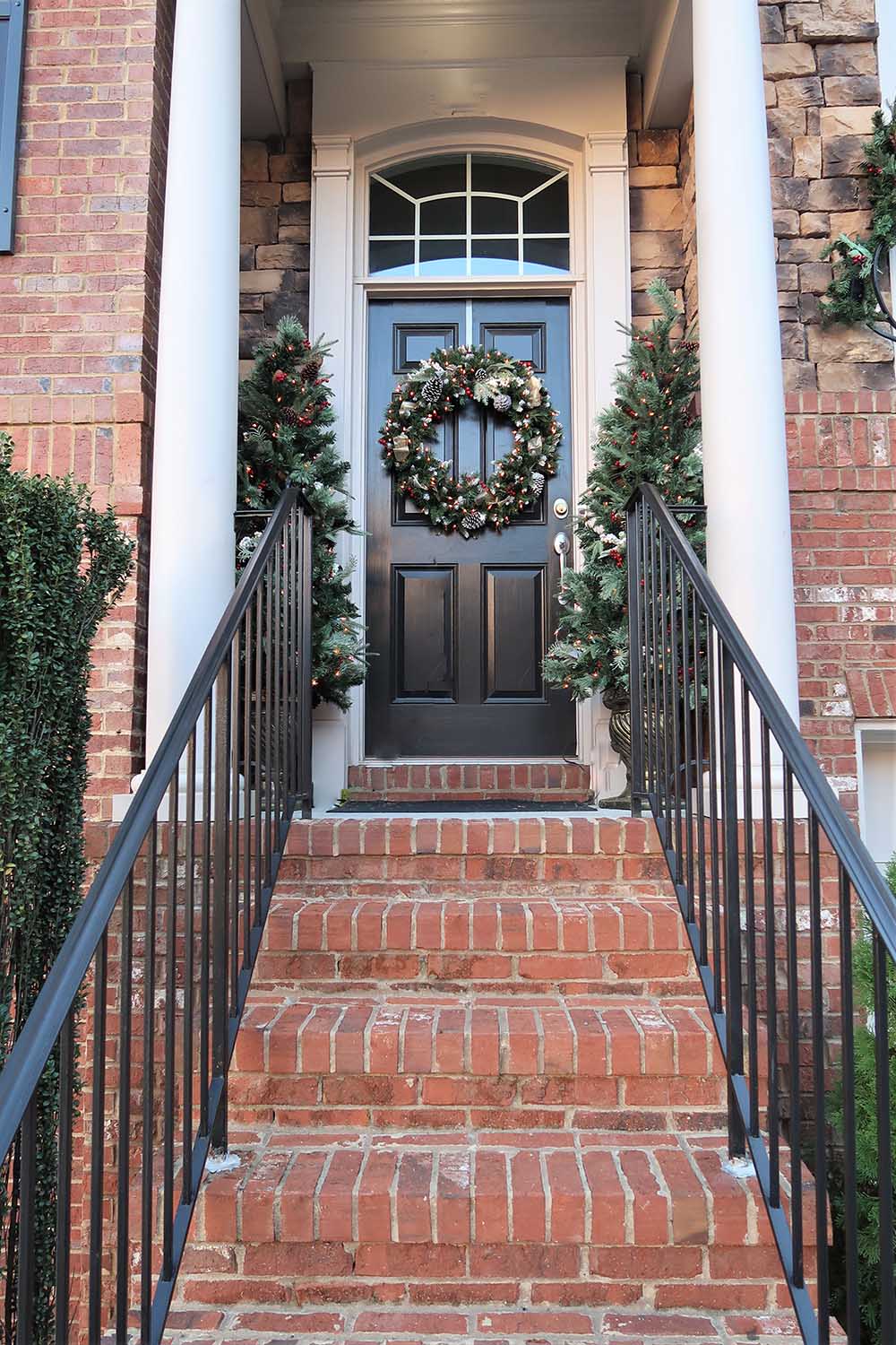 Two pre-lit potted artificial Christmas trees decorate the sides of a front door.