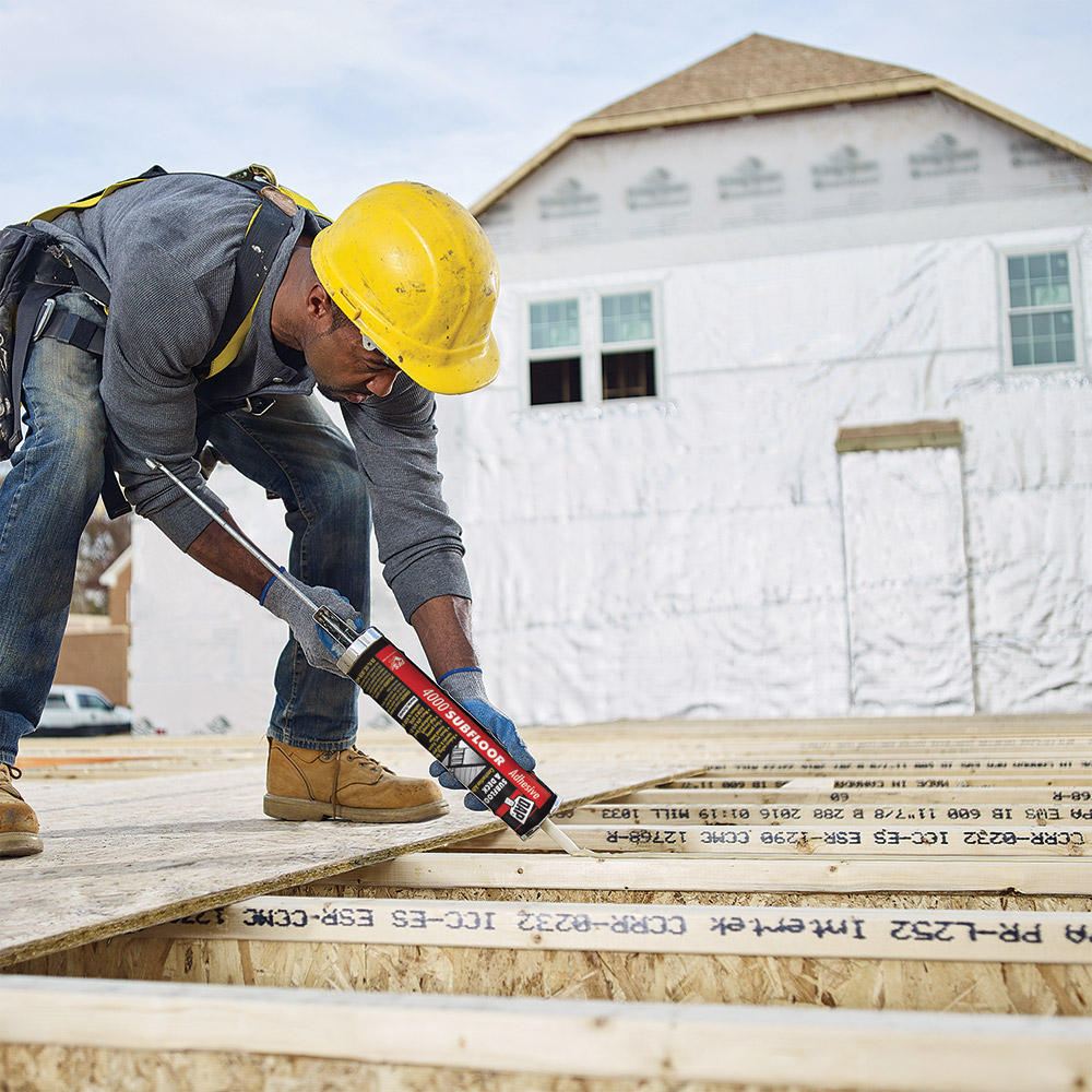 A person uses construction adhesive on a wood joist.