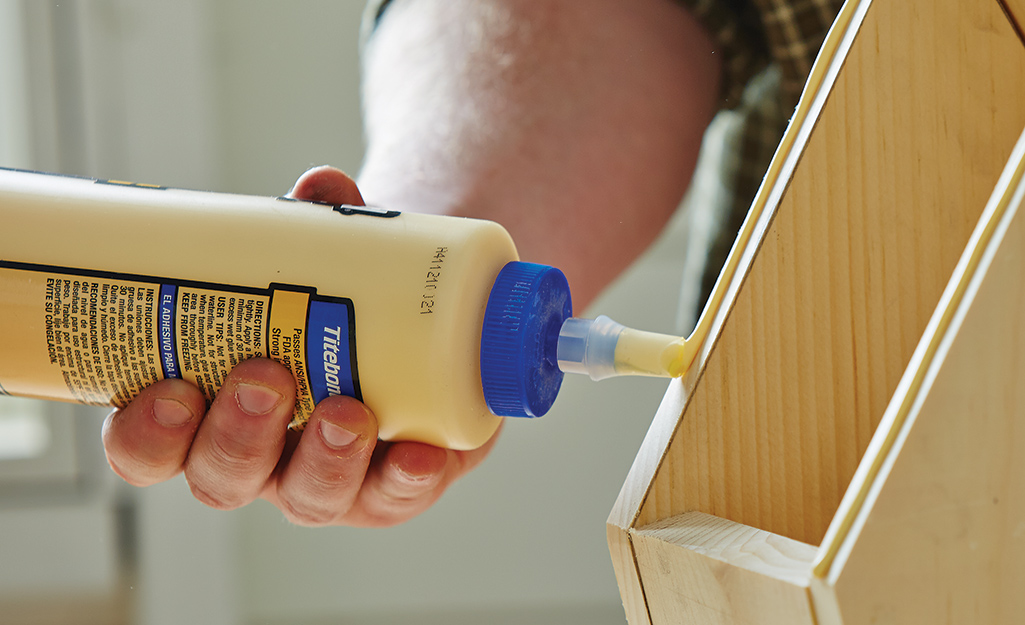 A person uses wood glue on a light wood box. 