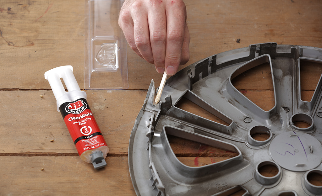 A person uses epoxy on a plastic wheel cover.