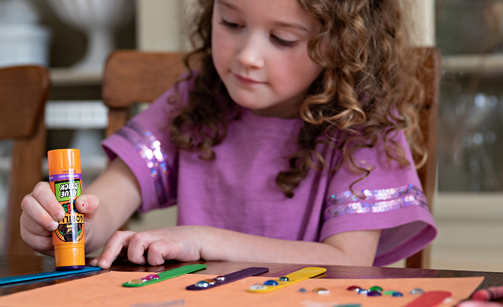 A child uses a glue stick to work on a craft project.