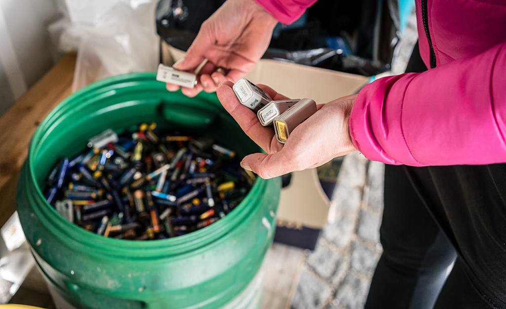 A person places batteries in a bucket for disposal.