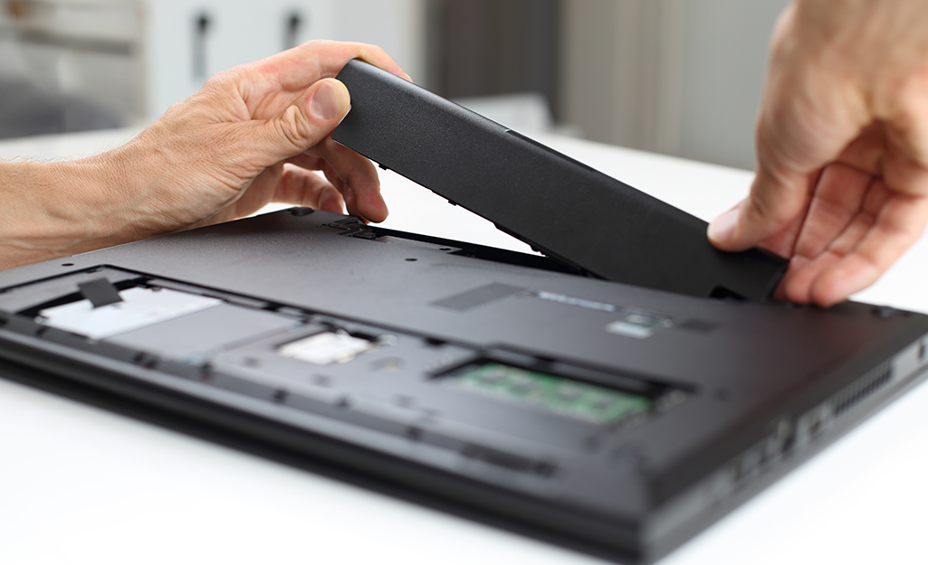 A person inserts a battery into a laptop computer.