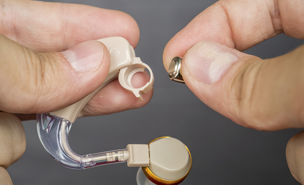 A person replaces a button cell battery used in a hearing aid.