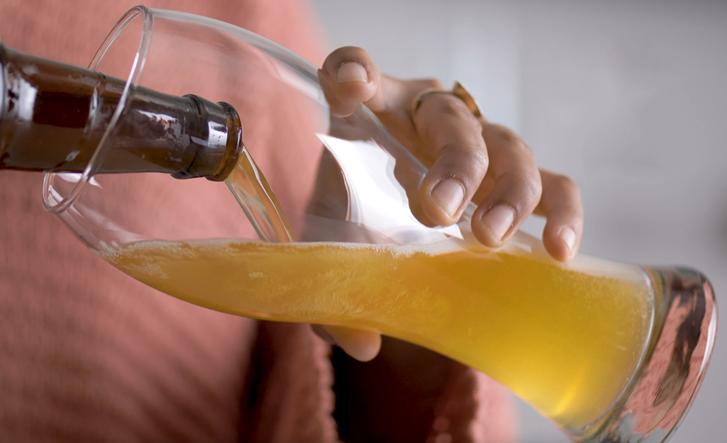 A person pouts beer from a bottle into a weitzen glass.