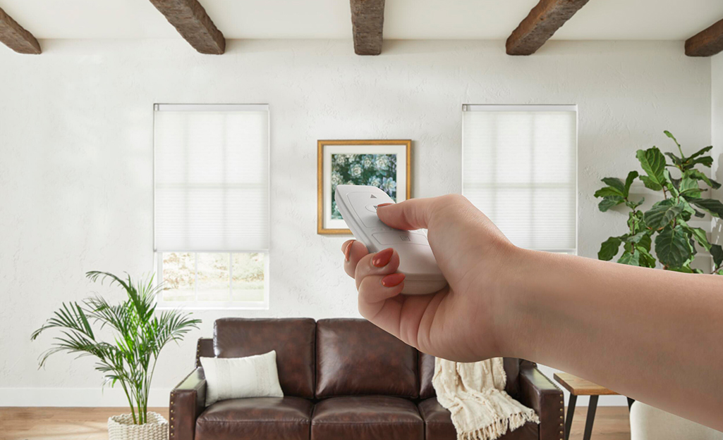 A person uses a remote control to operate motorized blinds.