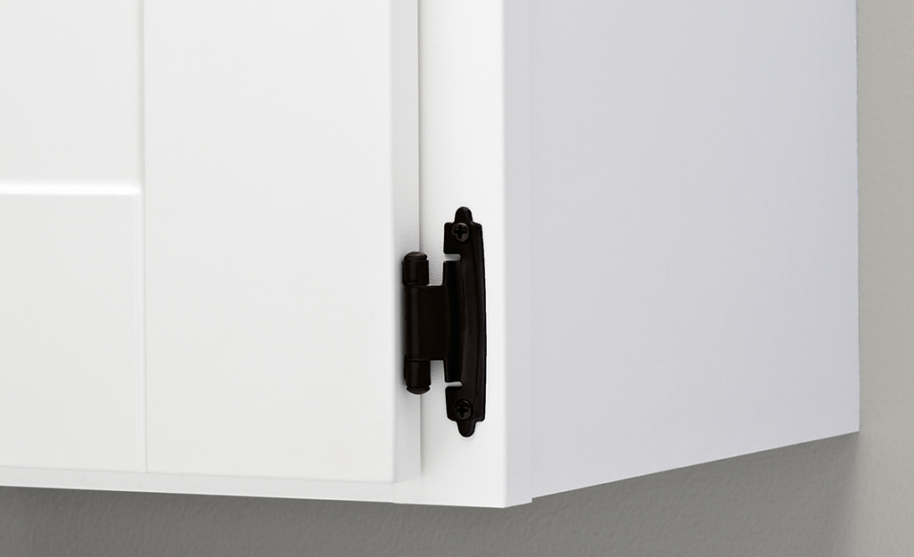 A black decorative hinge stands out on a white kitchen cabinet.