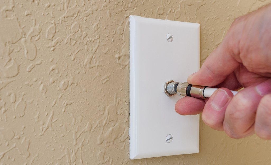 A person inserts a coaxial cable into a wall jack.