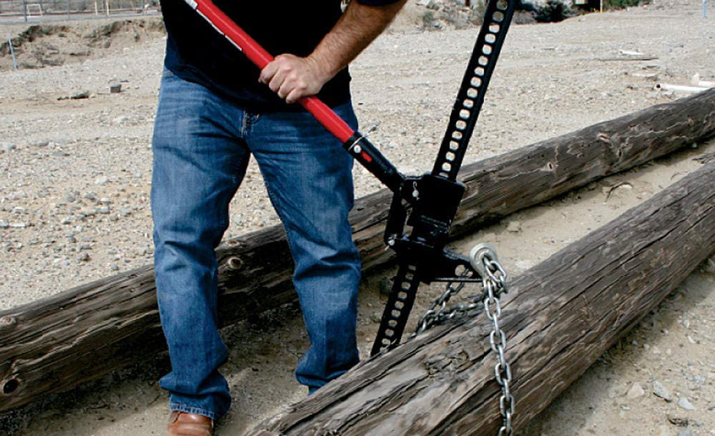 A man uses a farm jack to lift a log.