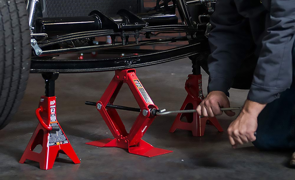 A person uses a scissor jack to jack up a car.