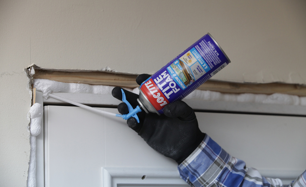 A person uses expandable foam caulk to seal a door frame