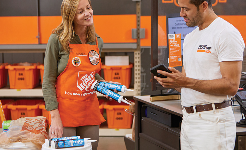 A Home Depot Store Associate holding caulk cartridges and helping a customer.