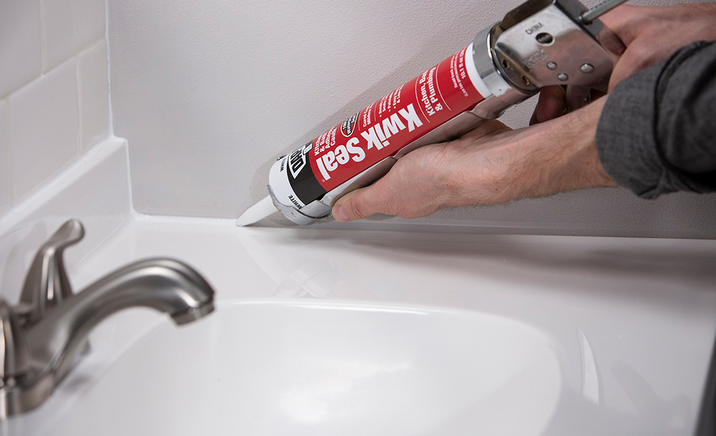 A person running a caulk bead on a kitchen backsplash.