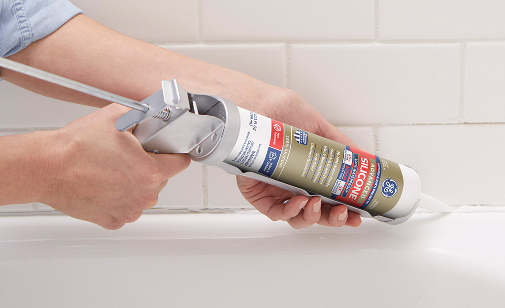 Person using a caulk gun with a silicone caulk cartridge in a tub