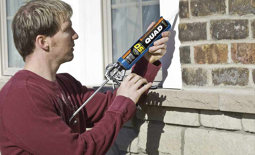 A person using caulk to seal a window frame and trim