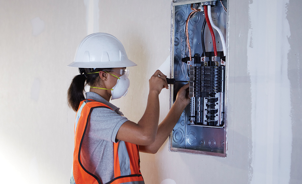 A person wearing a headlamp adjusts a circuit breaker in an electrical panel.