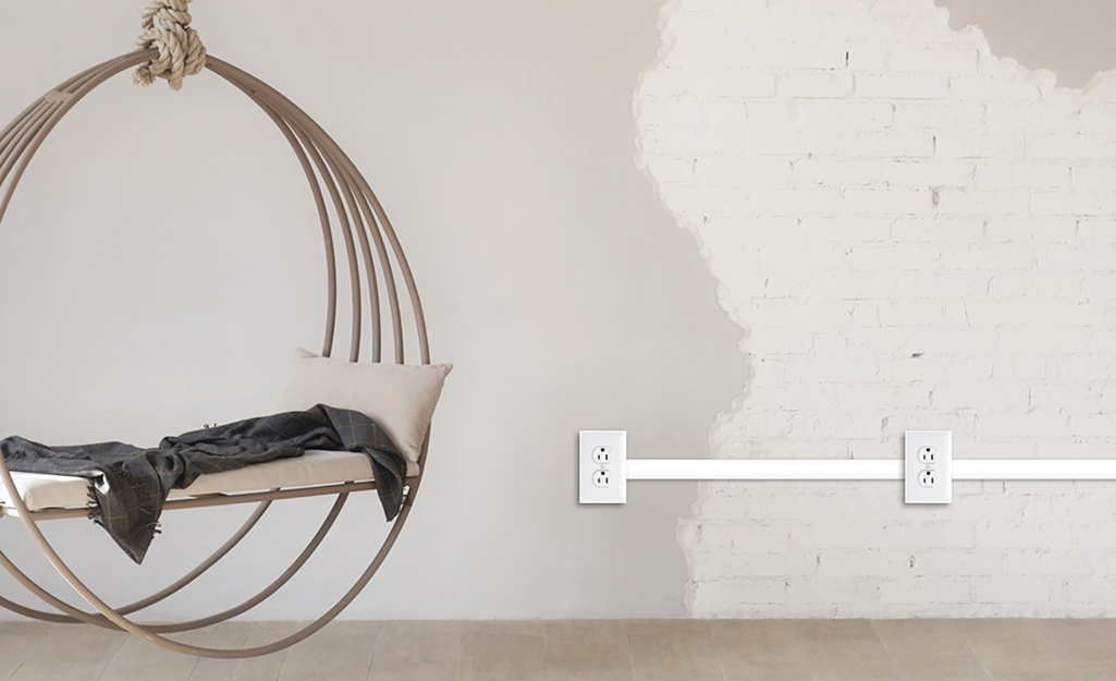 A swing chair hangs next to two outlets connected by conduit along a painted brick wall.