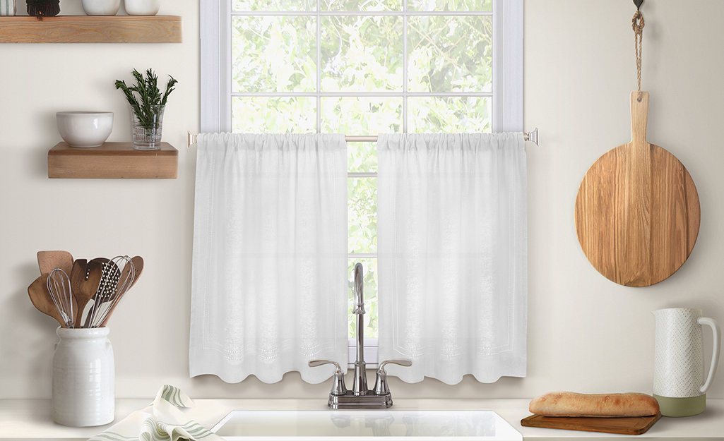 Cafe curtains hanging over a kitchen sink.