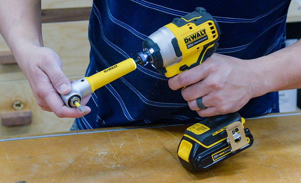 A person attaches a drill bit extender to a drill.