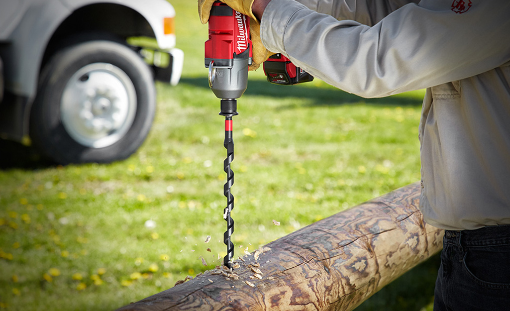 Someone using an auger drill bit on a log. Someone using an auger drill bit on a log.