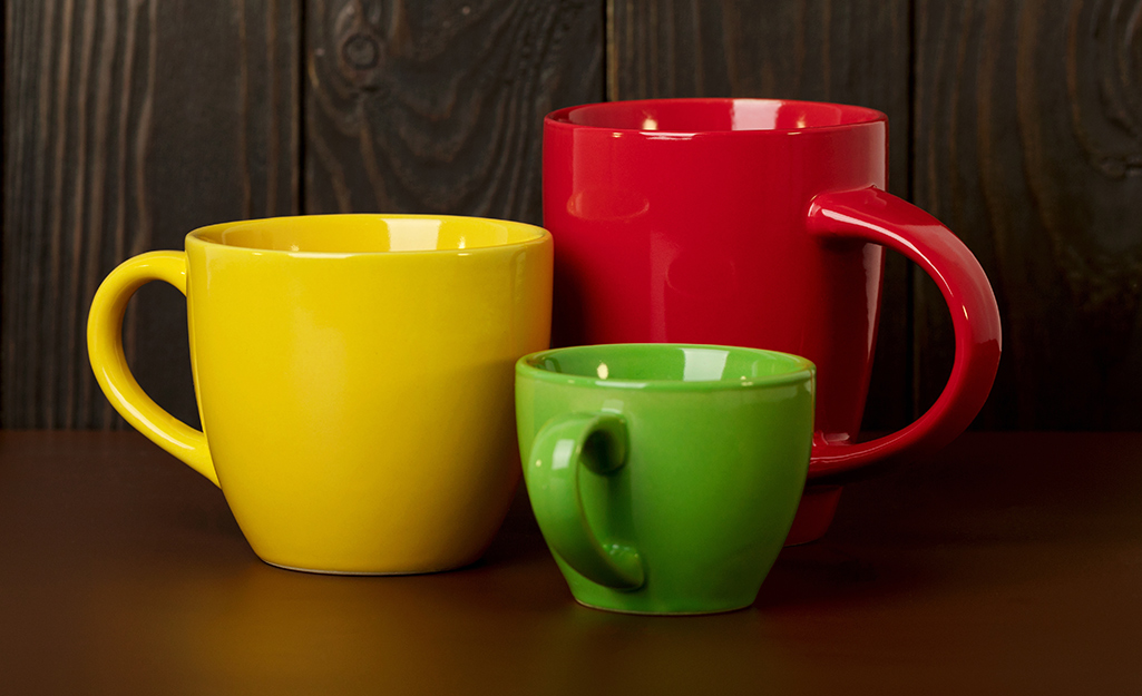 A yellow coffee mug, a red coffee mug and a green coffee mug sit on a dark background.
