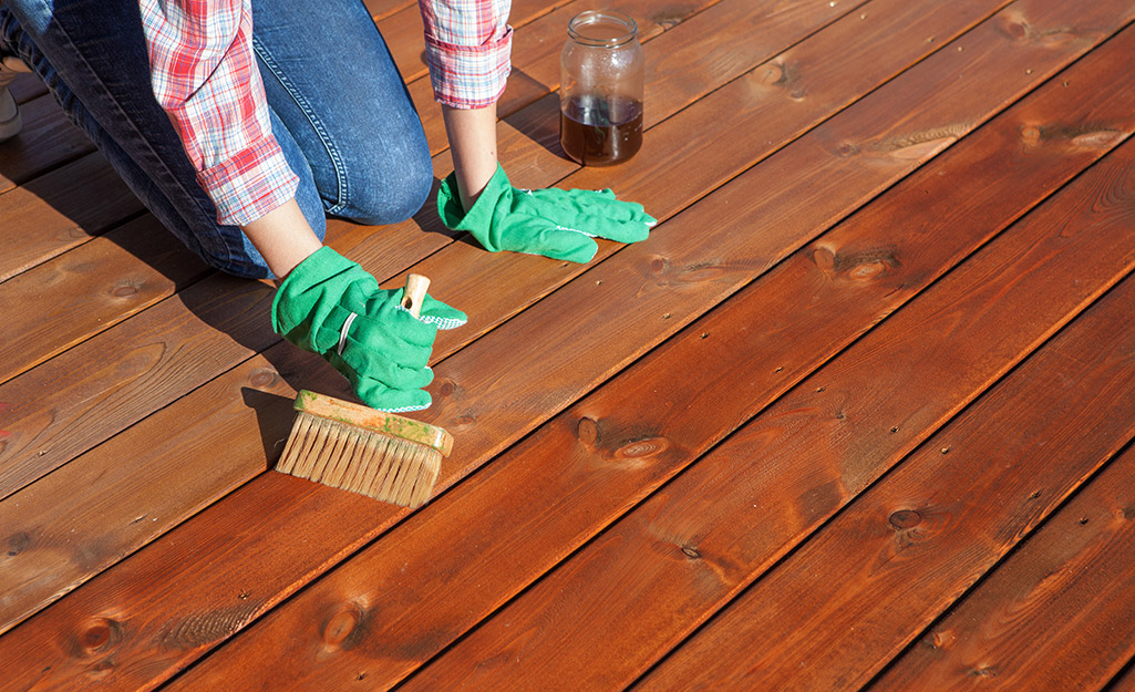 A person using an exterior wood sealer on a deck.