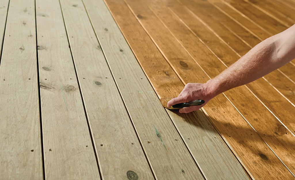 A person waterproofing a deck with a tinted exterior wood sealer.