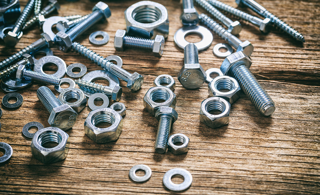 Assorted types of nuts, bolts and washers on a wooden surface.