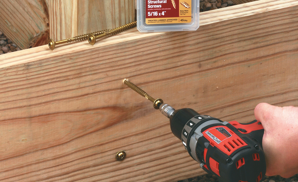 A power drill drives wood screws into an outdoor deck.