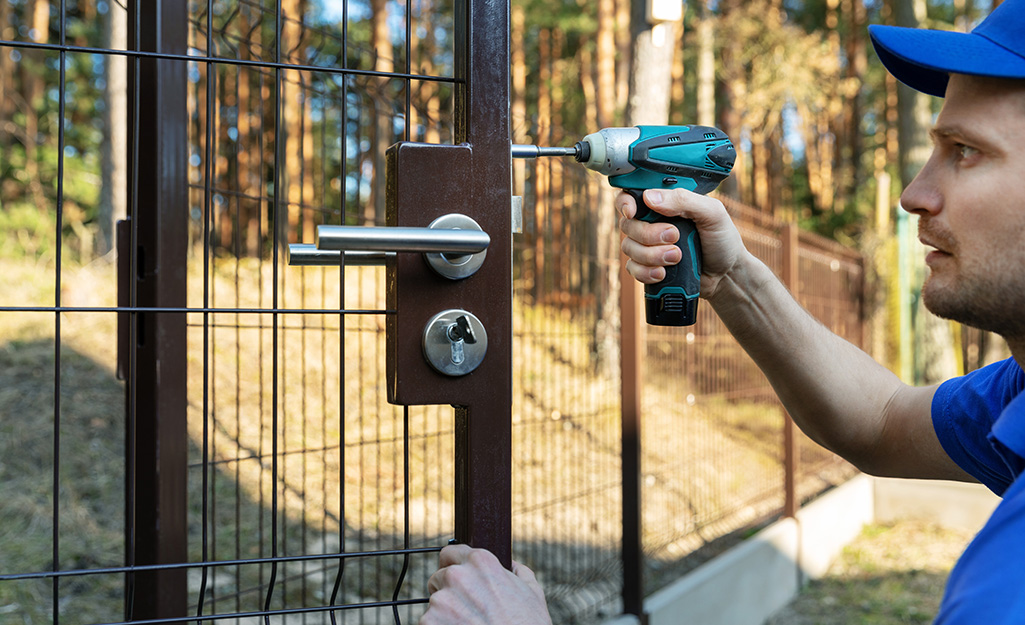 A person installing a gate on a fence.