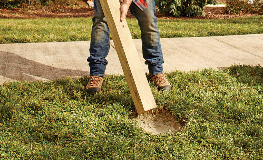 A person installing a fence post in a post hole filled with cement.