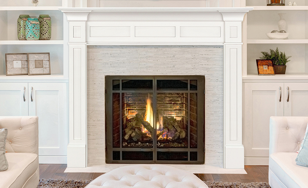 Two built-in bookshelves with lower cabinets stand on either side of a lit fireplace of painted brick and a white mantel.