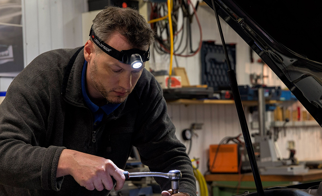 A man wears a headlamp flashlight to fix a car engine. A man wears a headlamp flashlight to fix a car engine.
