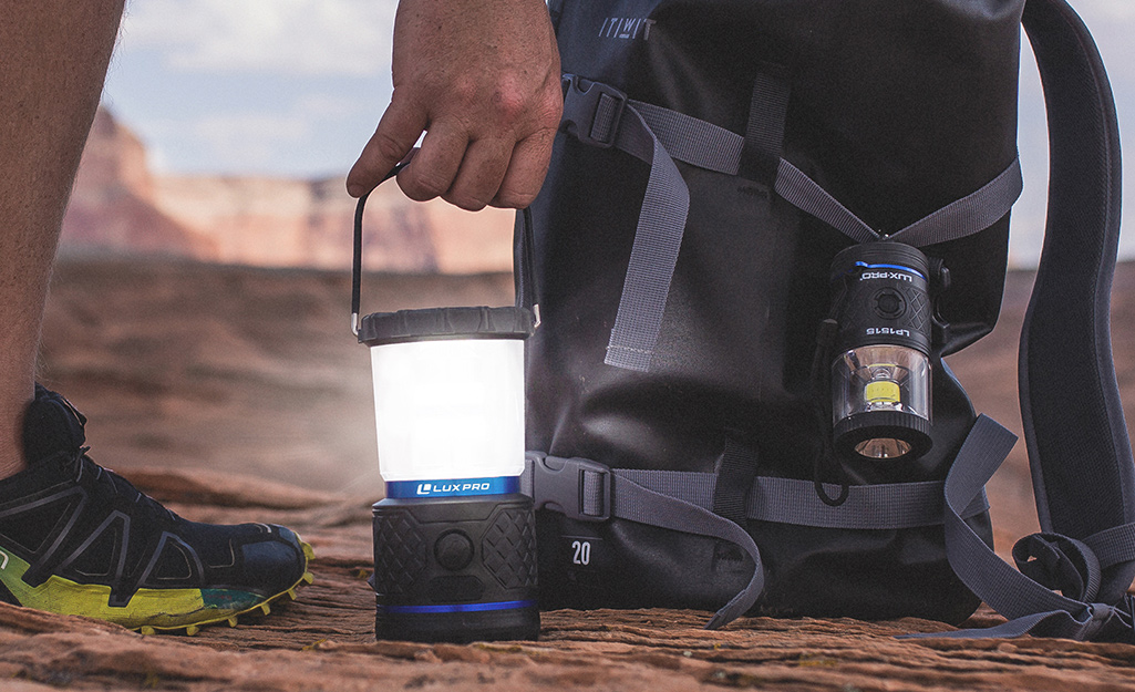 A lantern flashlight powered on is used by a hiker. A lantern flashlight powered on is used by a hiker.