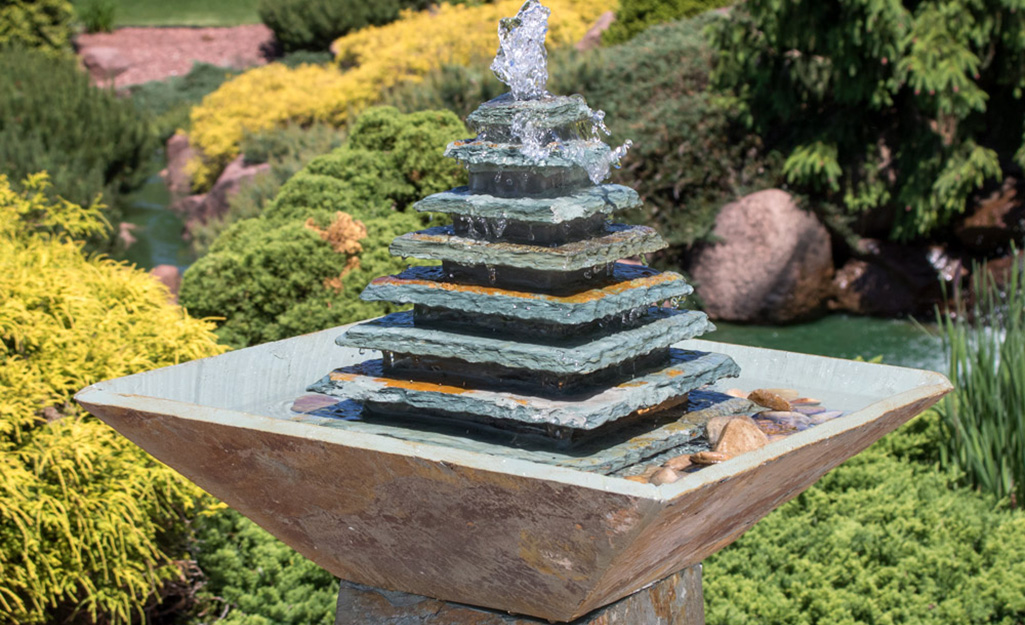 An outdoor water fountain in a flower bed.